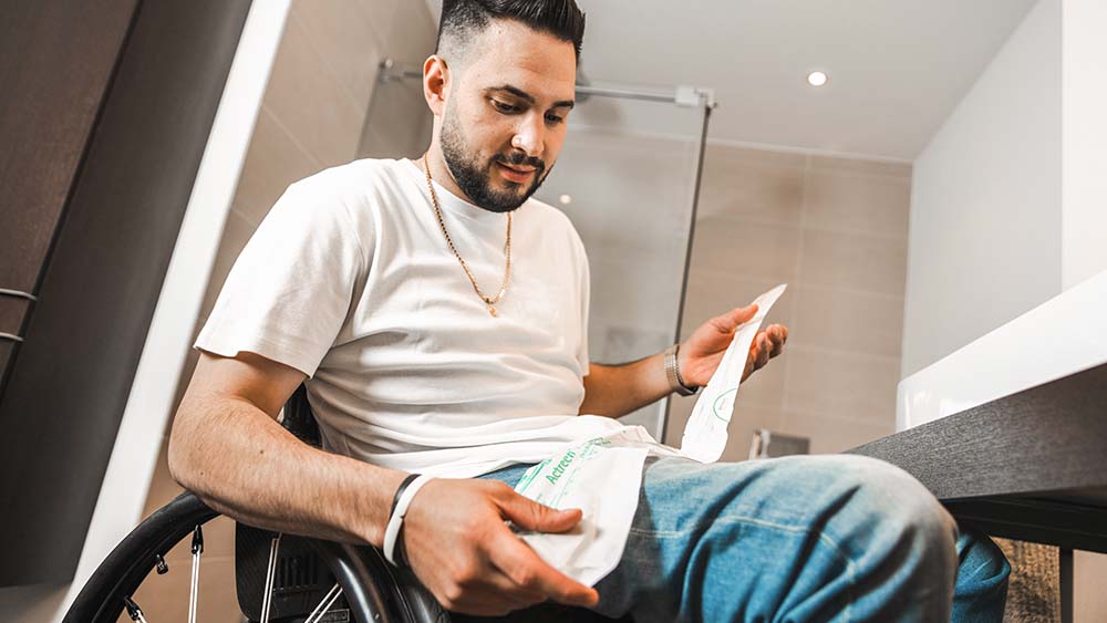 Un paciente sentado en una silla de ruedas sosteniendo una bolsa de catéter B. Braun.