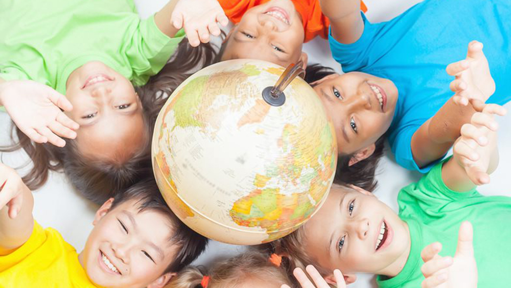 Niños sonriendo tumbados alrededor de un globo terráqueo en el suelo estirando los brazos hacia arriba.
