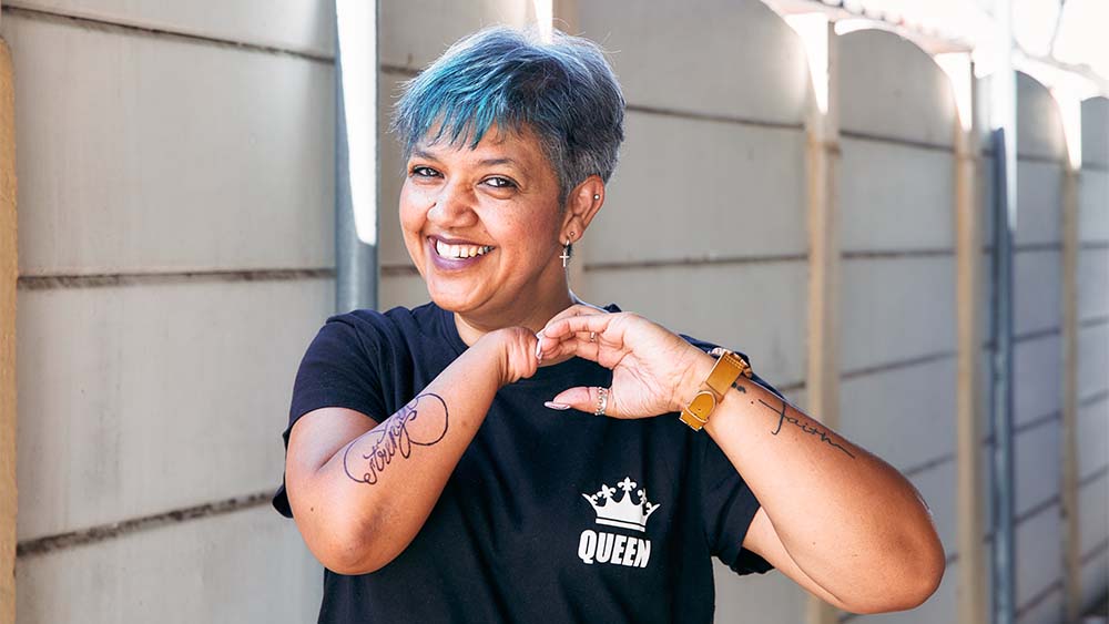 Una mujer sin mano derecha, pelo azul y tatuajes sonríe, irradia confianza y autoexpresión. 